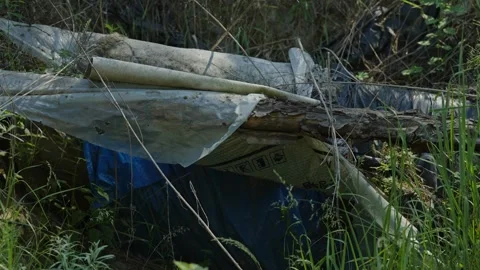 Close-up shot of discarded plastic tarps and debris in tall grass Stock Footage 337389200