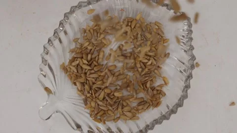 Close shot of falling sunflower seeds into transparent glass bowl Video stock 160885609