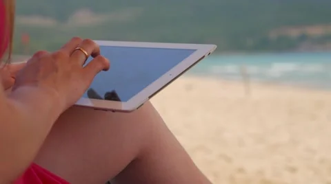 Close-up shot of female hands working on touch pad against background of beach 库存影片 63598012