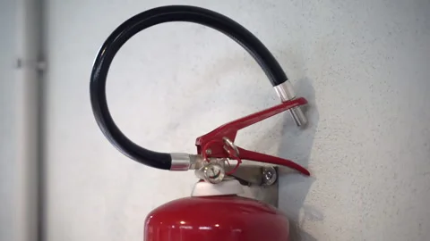Close-up shot of fire extinguisher handle with nozzle hanging on white wall Vidéo 250484396
