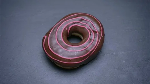 Close-up shot of glazed brown donut spinning around and bitten on gray table Video stock 102327392