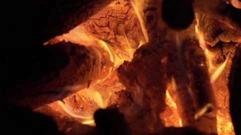 Close-up shot of glowing orange flames flickering between burning wooden logs Stock Footage 339675564