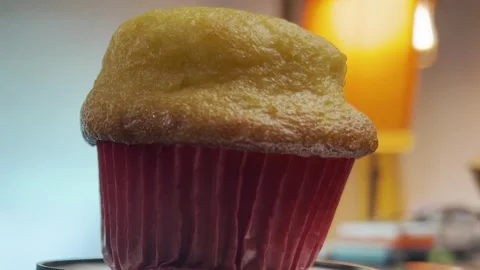 A close-up shot of a golden muffin in a red wrapper with a blurred lamp in the Stock Footage 296569958