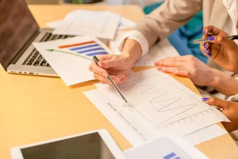 Close-up shot of graphics placed on the table and women's hands on them Stock Photos