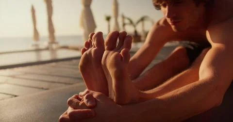 Close-up shot of a guy stretching his legs and body while doing yoga on a sunny Stock Footage 249606261