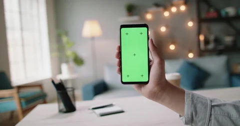 Close up shot of hand of guy holding a smartphone in cozy living room. A green Stock Footage 137906482