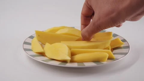 Close up shot of hand picking fresh yellow mango slices on striped plate wi.. Stock Footage 332031947