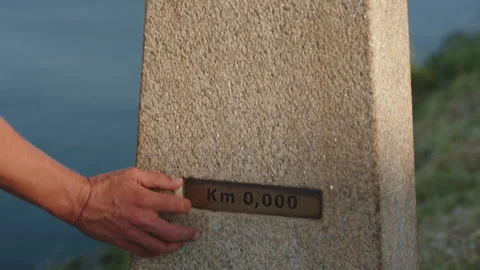 Close-up shot of a hand touching a stone marker inscribed with "Km 0,000," on 動画素材 344212324