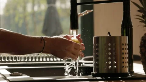 A  close-up shot of hands gently rinsing fresh lemon under a stream of water Video stock 304588008