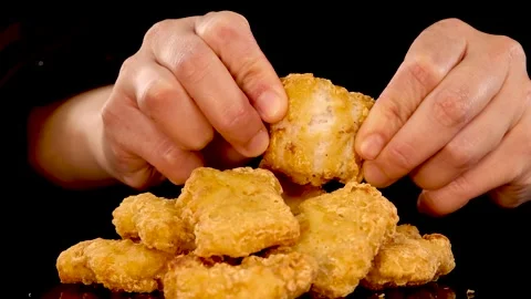 A close-up shot of hands reaching for and breaking apart a crispy chicken n.. Vídeo Stock 333486404