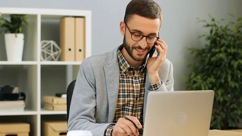 Close up shot of a happy man in glasses sitting at the office desk, talking on Stock Footage 80925286