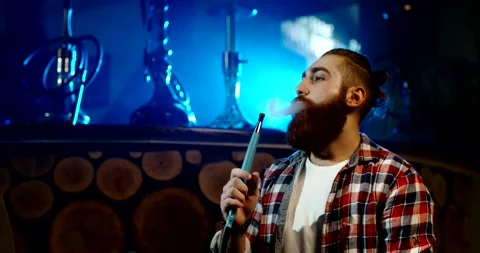 Close up shot of hipster bearded guy smoking a shisha in a club, exhaling a fog Stock Footage 133356867