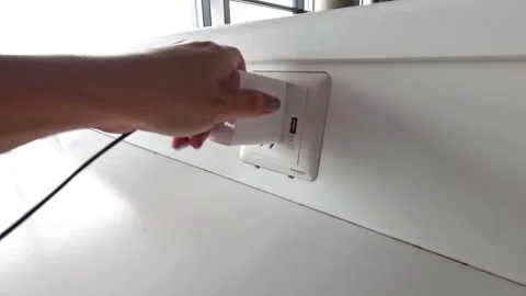 Close up shot of human hand plugging white power adapter into wall socket o.. Video stock 332757415