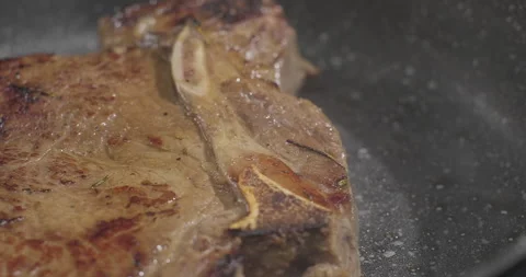 Close-up shot of juicy beef t-bone steak cooking on a frying pan. Slow motion Stock Footage 250802013