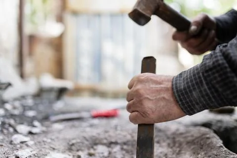 Close-up shot of a man breaking down a wall using a hammer and chisel. Stock Photos