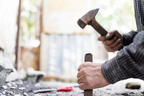 Close-up shot of a man breaking down a wall using a hammer and chisel. Stock Photos