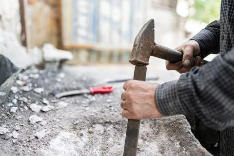 Close-up shot of a man breaking down a wall using a hammer and chisel. Stock Photos