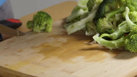 Close shot of a man chopping broccoli on the board, dark male hands cutting it Stock Footage 150373662