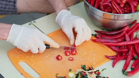 Close up shot of a man cutting red hot peppers, wearing white latex gloves. Stock Footage 286372314