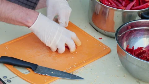 Close up shot of a man cutting red hot peppers, wearing white latex gloves. Video stock 286416224