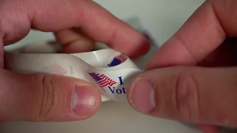 Close up shot of Man getting his I Voted sticker from a roll after voting in USA Stock Footage 141215185