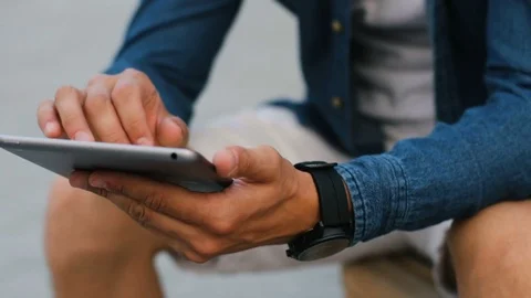 Close up shot of man hands using tablet computer while sitting on the bench in Stock Footage 78585148