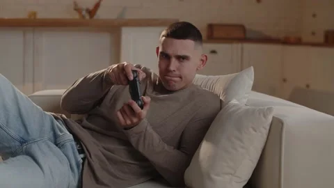 Close-up shot of a man lying on a couch with a gamepad in his hands who is Video stock 234177690