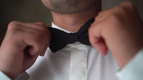Close shot of man putting on a bowtie. Young adult in white shirt wearing an Stock Footage 148736099