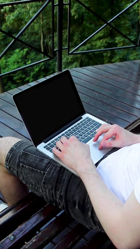 Close up shot of a man in a white t-shirt and dark shorts working on a laptop Stock Footage 313244408