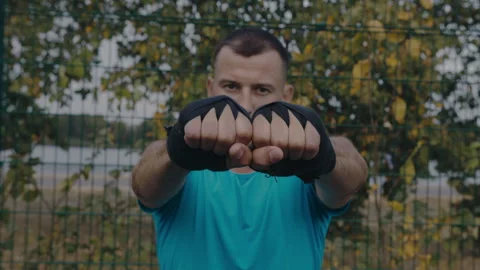 Close-up shot of a man with wraps on his arms boxing with a shadow outdoors  動画素材 251781114