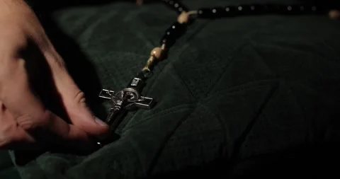 Close-up shot of a man's hand placing a rosary with Jesus Christ on a dark Stock Footage 296141960