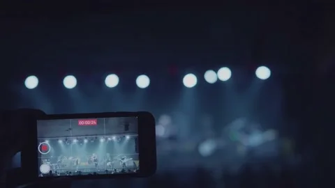 A close-up shot of a man's hand is taking video for a music band on stage. Video stock 145125606