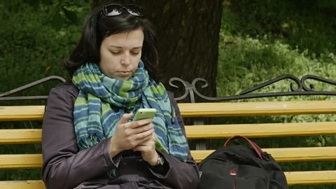 Close up shot of a park bench and the woman sitting and using mobile phone Stock-Footage 103257786