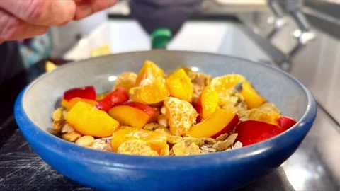 Close up shot of person in kitchen preparing of bowl of cereal with fruit Stock Footage 340434335
