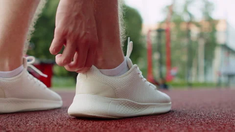 Close up shot of a person putting on a white running shoes on an outdoor sp.. Video stock 341458047