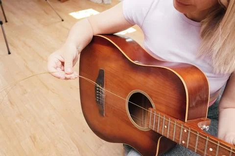 A close-up shot of a person's hands installing new bronze strings on a brown  Stock-Fotos
