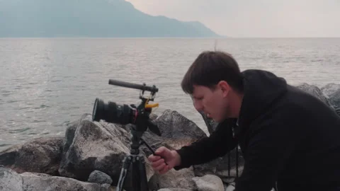 Close up shot of photographer setting up a camera on a tripod next to Lake Видео 333180856
