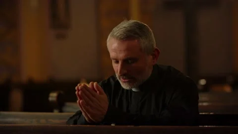 Close-up shot of a priest sitting on a bench in a church. A priest in a black Stock Footage 234897576