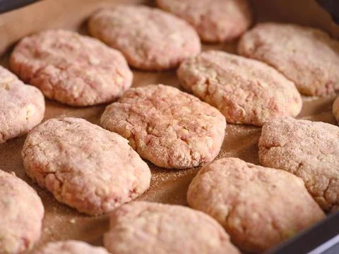 Close-up shot of raw breaded meat cutlets on a parchment paper on a baking tr Stock Photos