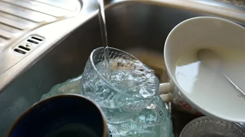 A close-up shot of running water pouring directly into dirty dishes in the sink. Stock Footage 314468480