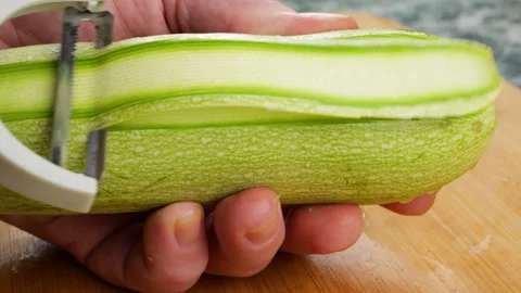 A close-up shot shows a chef peeling a fresh green zucchini. 스톡 동영상 341538256
