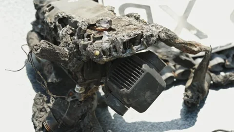 A close-up shot shows a completely burnt and melted quadcopter drone with Stock Footage 339910754