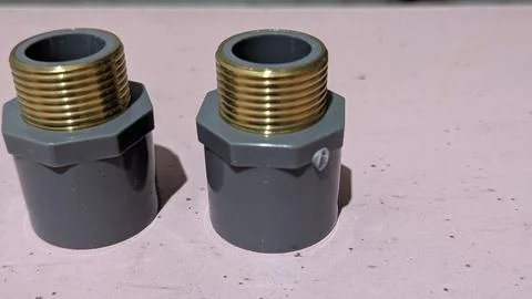 A close up shot shows two grey PVC pipe adapter fittings with golden brass .. Stock Photos