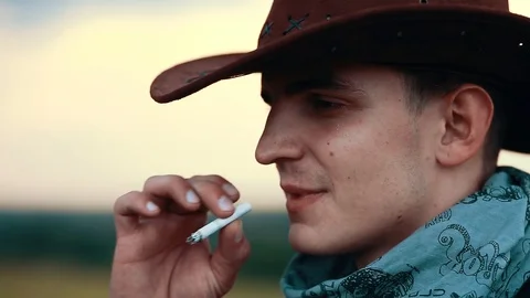 Close up shot of side young cowboy smoking cigar look at camera serious on field Stock Footage 121065248