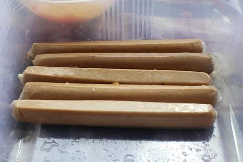 A close-up shot of six pre-packaged light brown sausages arranged horizontall Stock Photos