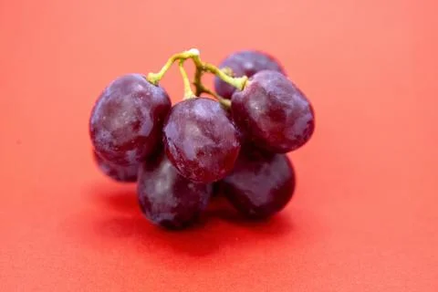 A close-up shot of a small bunch of red grapes on a red background. Stock Photos