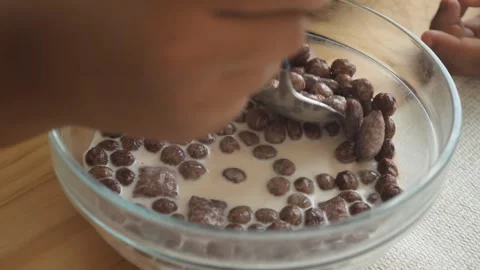 Close up shot of spoon scooping chocolate cereal with milk in bowl during b.. Видео 331836073