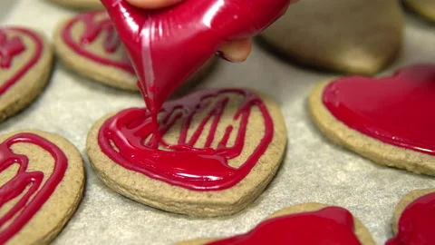 Close-up shot of squeezing red sweet frosting onto heart-shaped cookies. Making Video stock 146873102