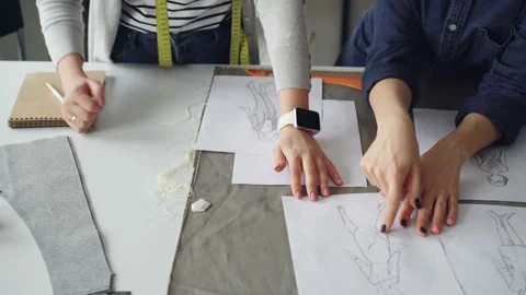 Close-up shot of tailors' hands going through sketches on sewing desk. Women are Stock Footage