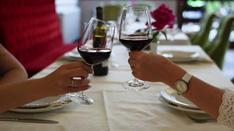 Close-up shot of two female hands cheering with glasses of red wine over a serve Stock Footage 336870485